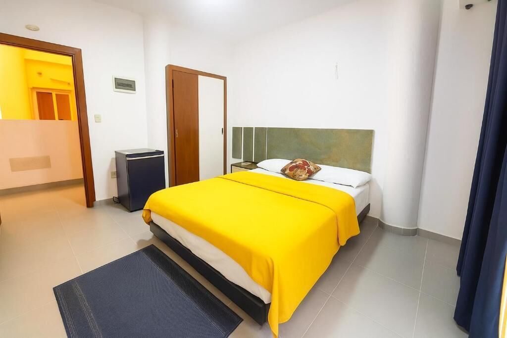 A hotel room with a bed, a desk, a chair, a wardrobe, and a small trash bin.