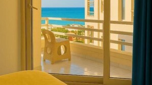 Habitación de hotel con puerta corrediza de vidrio que da a un balcón con vista al océano.