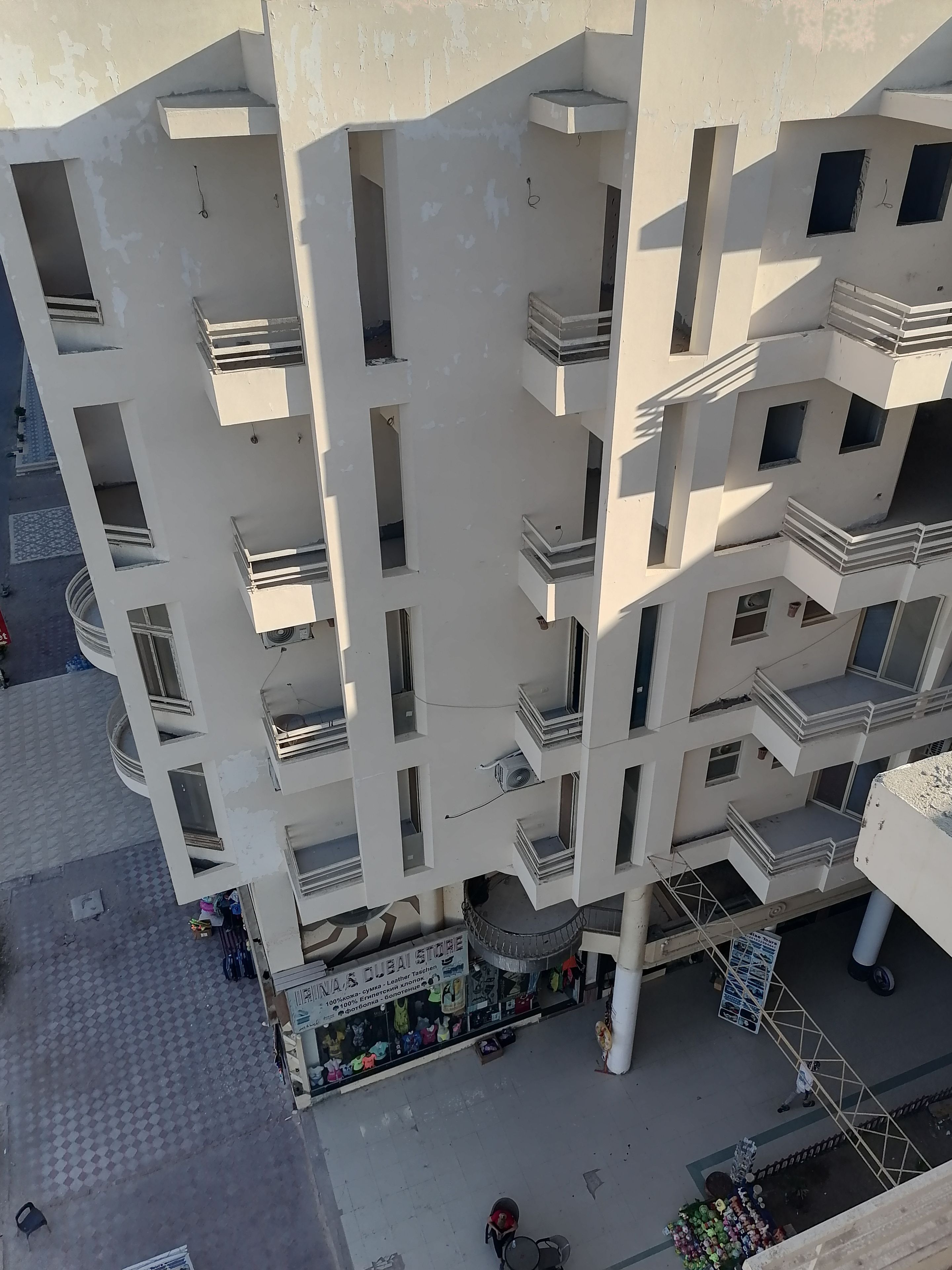A multi-story building with balconies, a ground-level shop, and a pedestrian area.