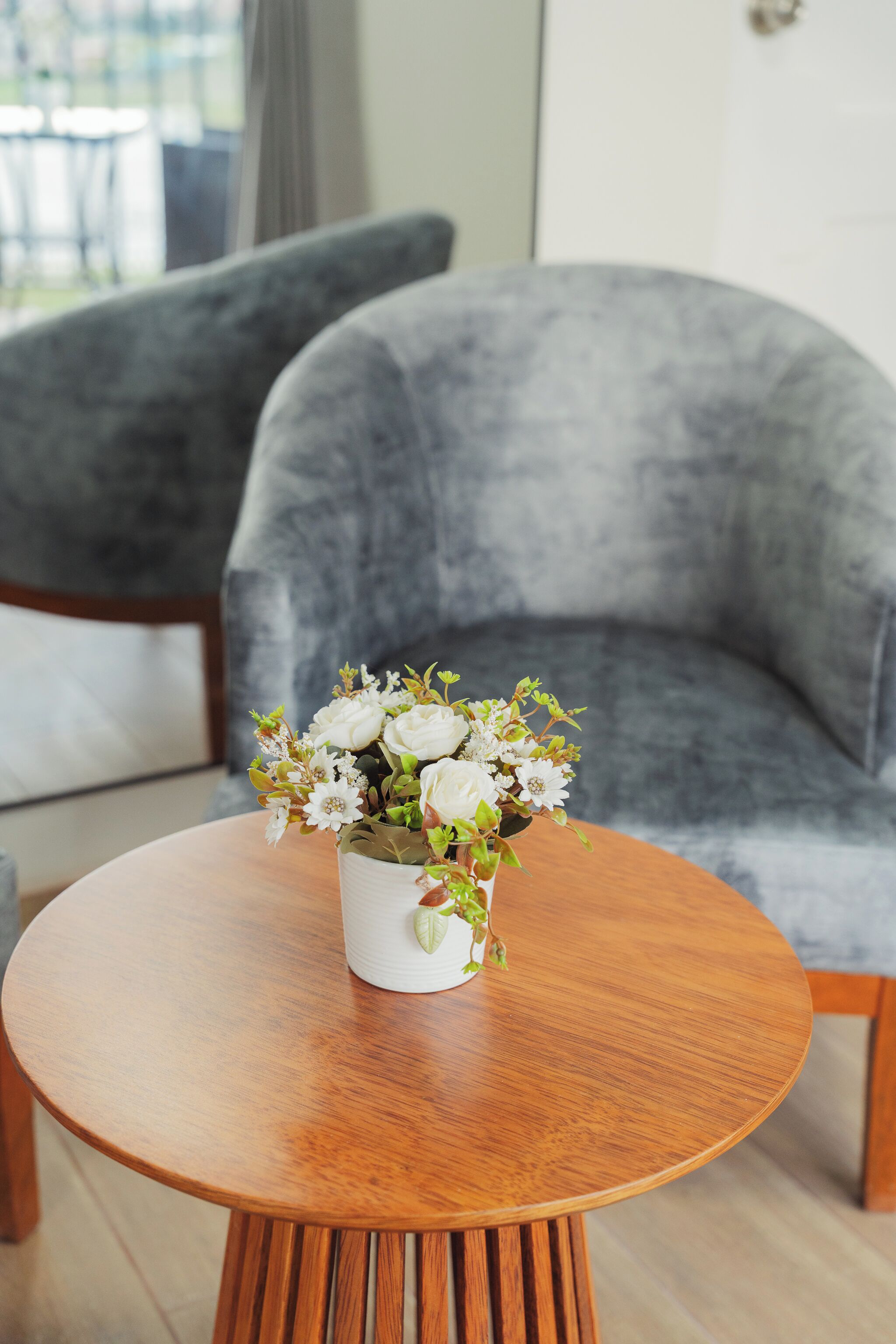 A round wooden table with a white vase containing white flowers.