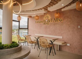 Un vestíbulo de hotel con sillas de mimbre, una mesa larga y un amplio ventanal con vistas a edificios y vegetación.