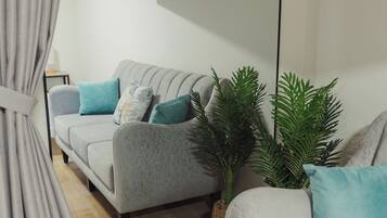 Een moderne woonkamer met een grijze bank, een flatscreen televisie aan de wand en een plant in een pot.