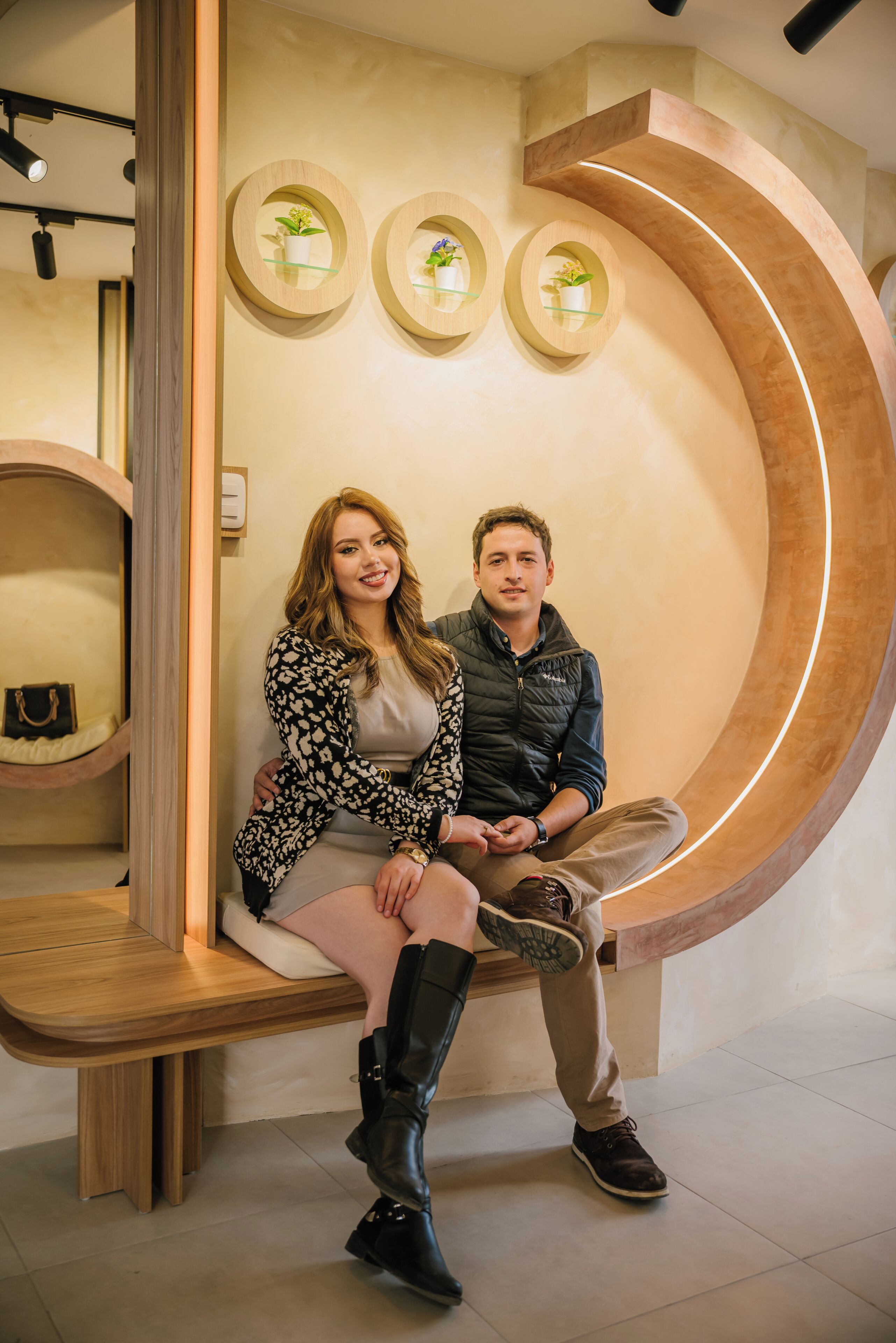 Um casal sentado em um banco em um interior moderno, com decorações circulares na parede e um banco de madeira.