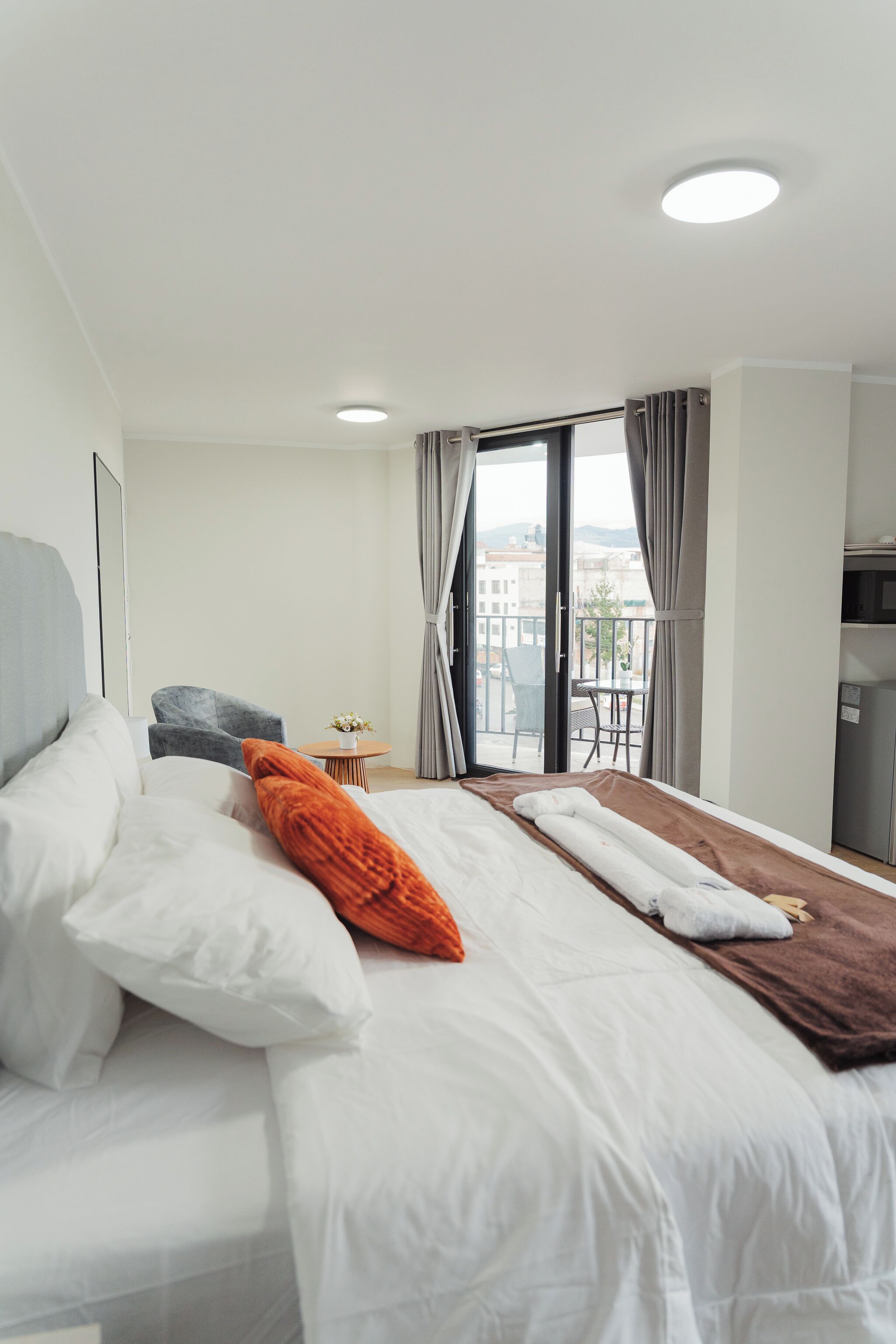 Habitación de hotel con cama, una mesita con un florero, una silla y un balcón con mesa y sillas.