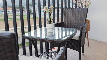 A balcony with a glass table and wicker chairs, overlooking a view of buildings and a distant landscape.