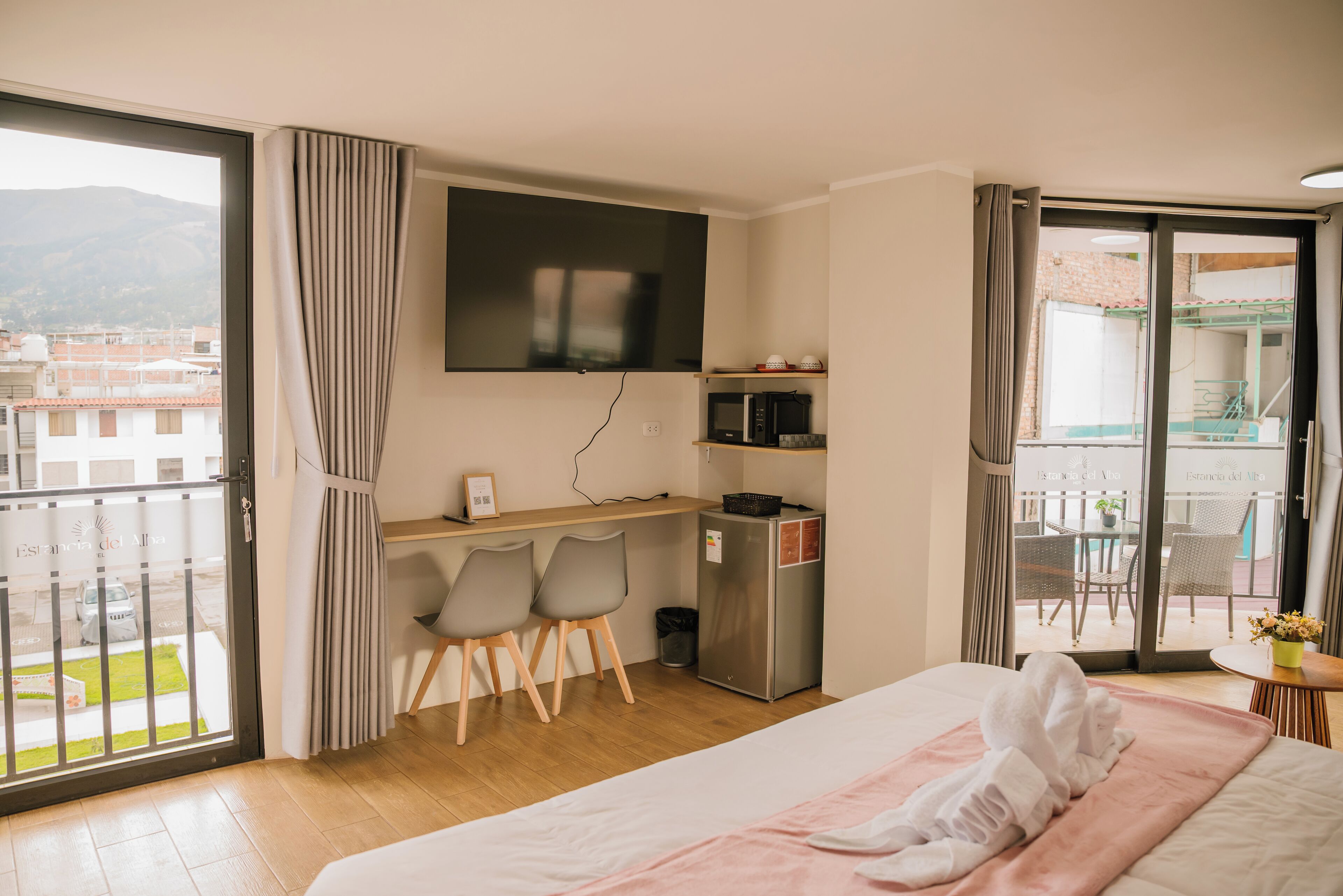 Une chambre d’hôtel équipée d’un lit, d’un bureau, de chaises, d’une télévision, d’un réfrigérateur et d’un balcon offrant une vue sur la ville.
