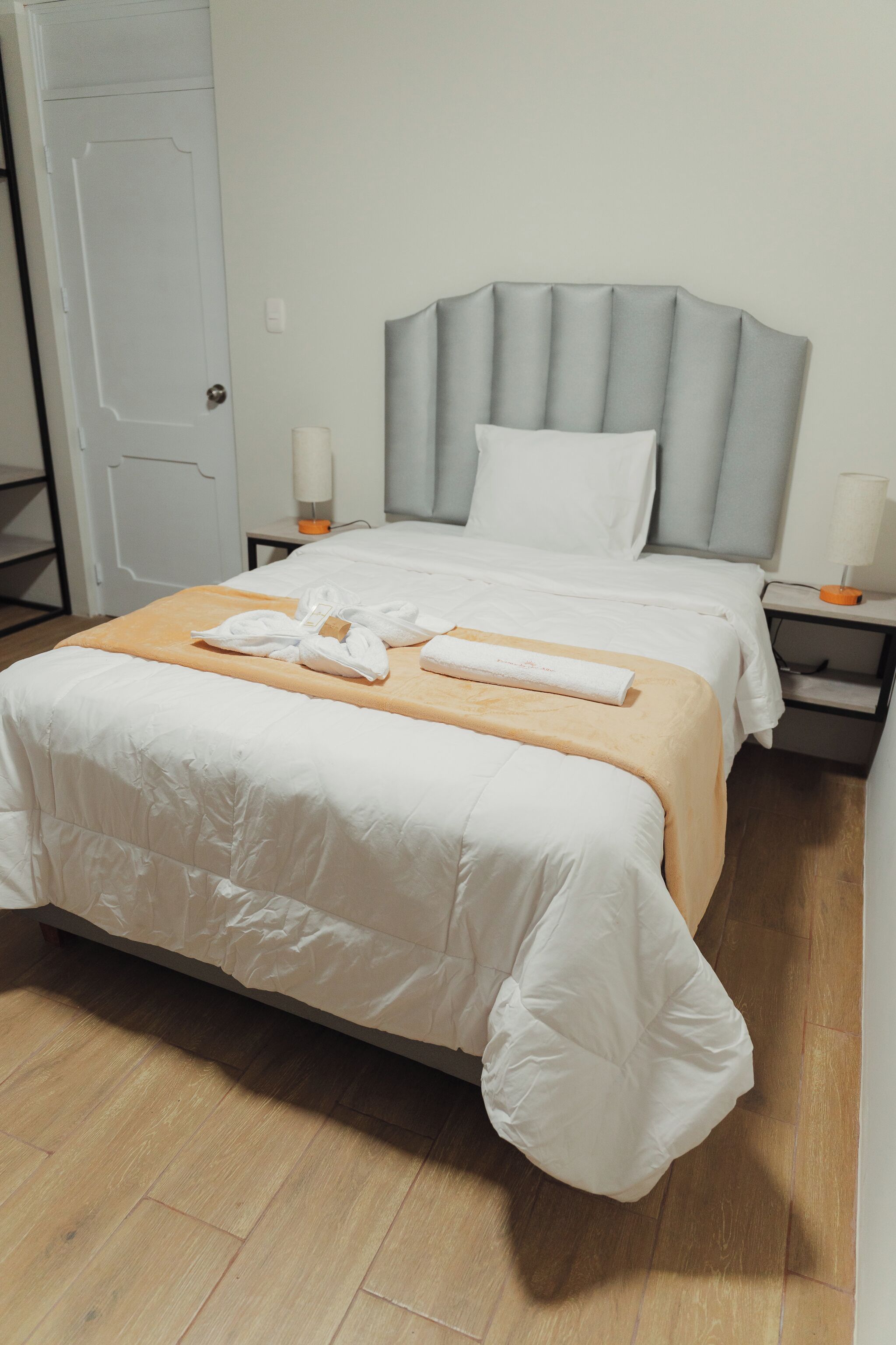 Una cama bien hecha con ropa blanca, un cabecero de madera y una mesita de noche con una lámpara.
