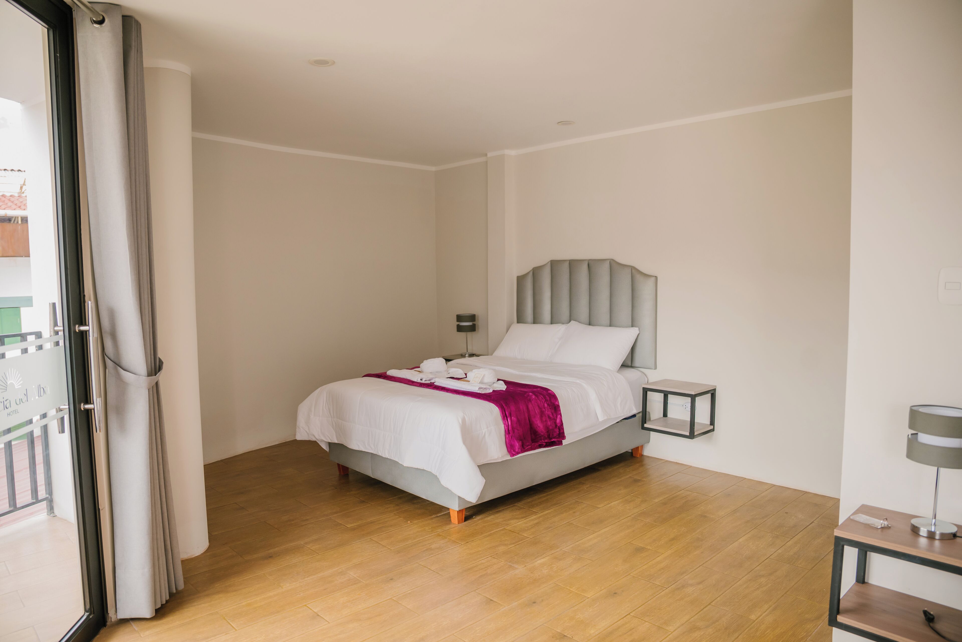 A bedroom with a bed, a bedside table, a nightstand, and a window with curtains.