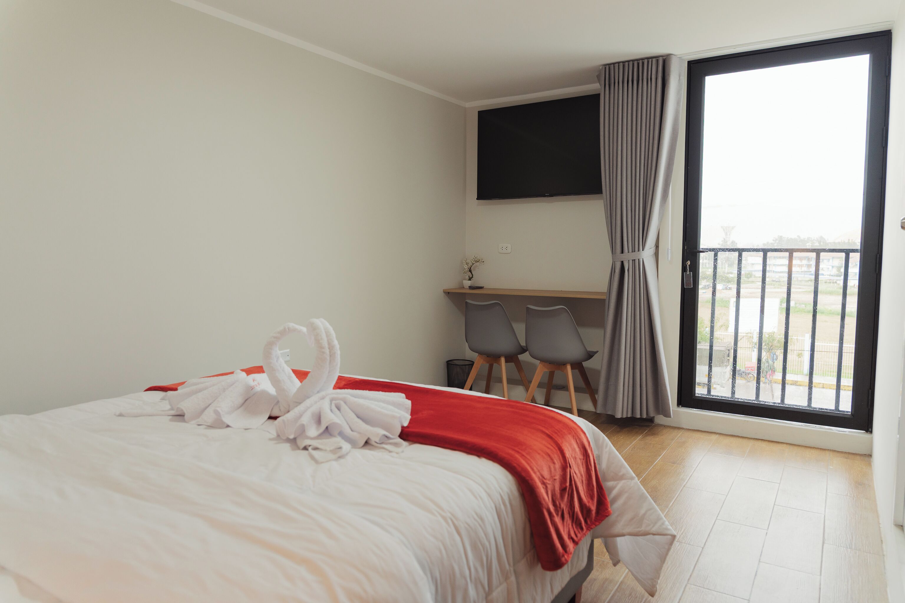 A hotel room with a bed, a desk with chairs, a TV, and a balcony with a view.