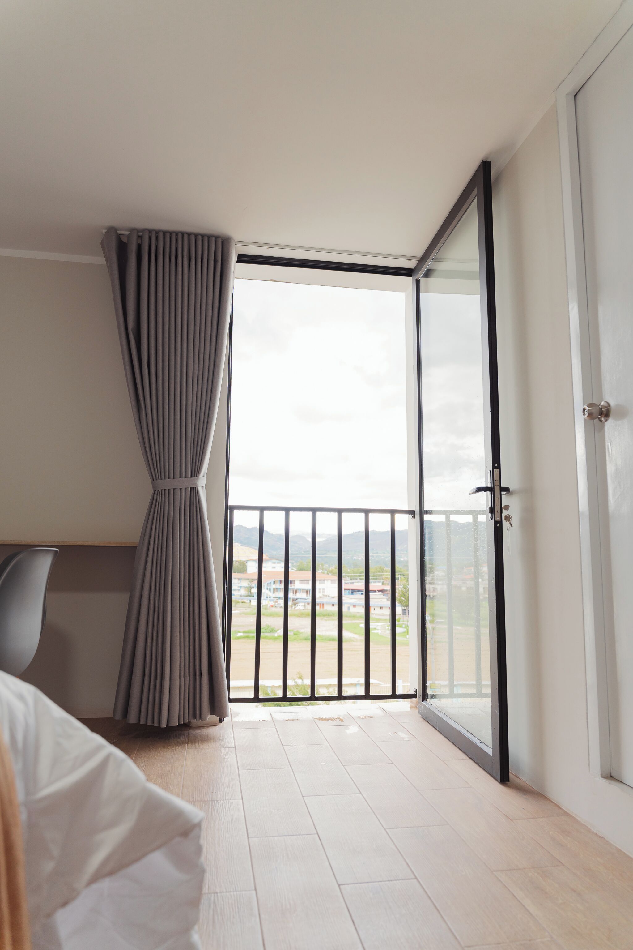 A hotel room with a balcony, a bed, a chair, and a view of the cityscape.