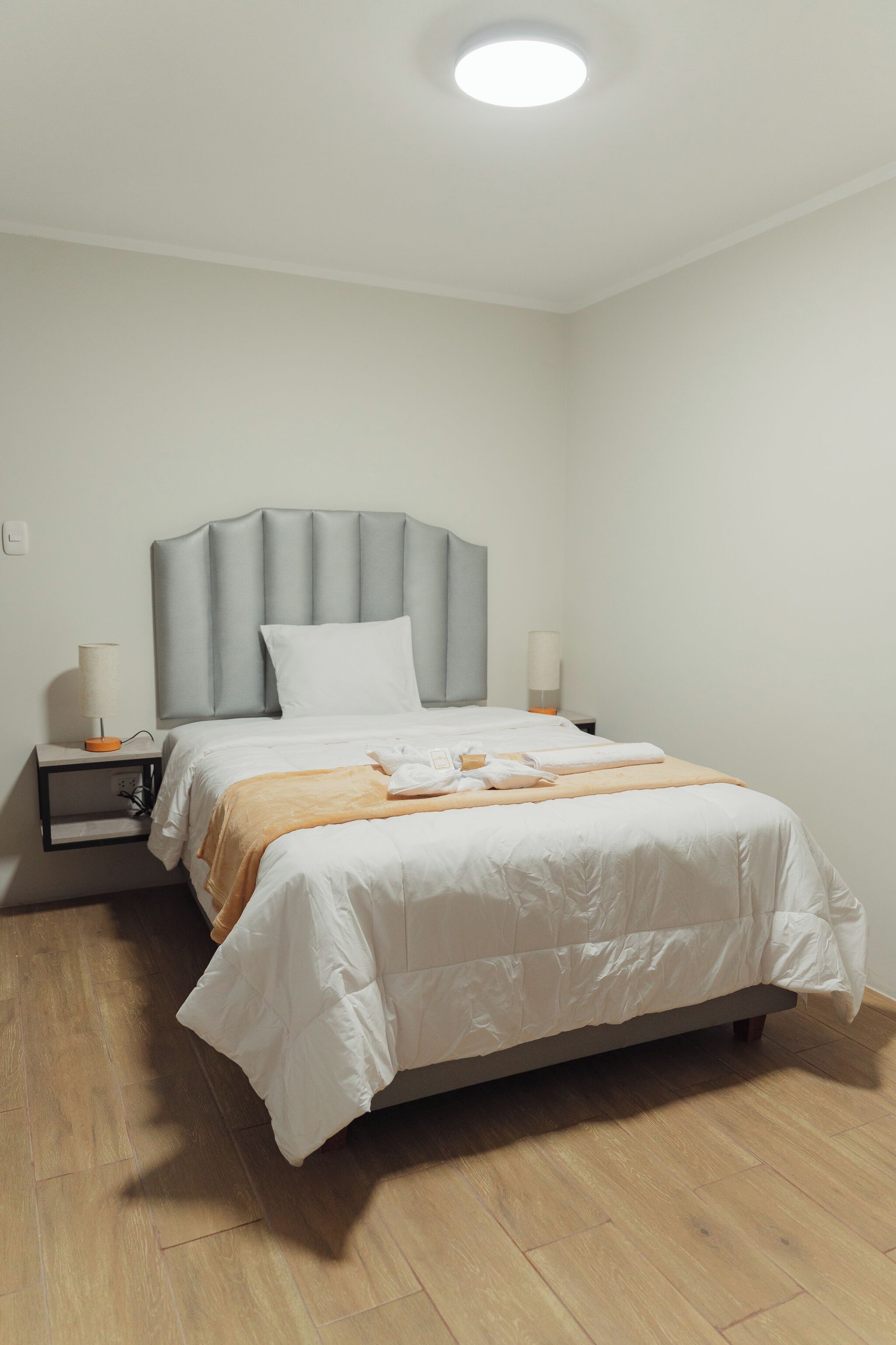 A neatly arranged bedroom with a bed, bedside tables, and a ceiling light.