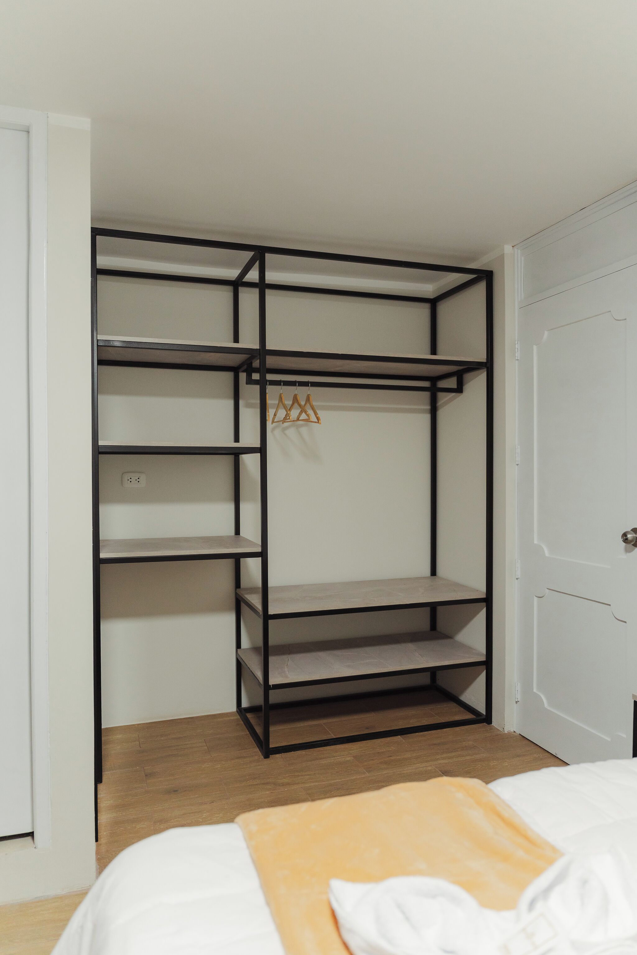A room with a bed, a white door, and a black metal wardrobe with multiple shelves.
