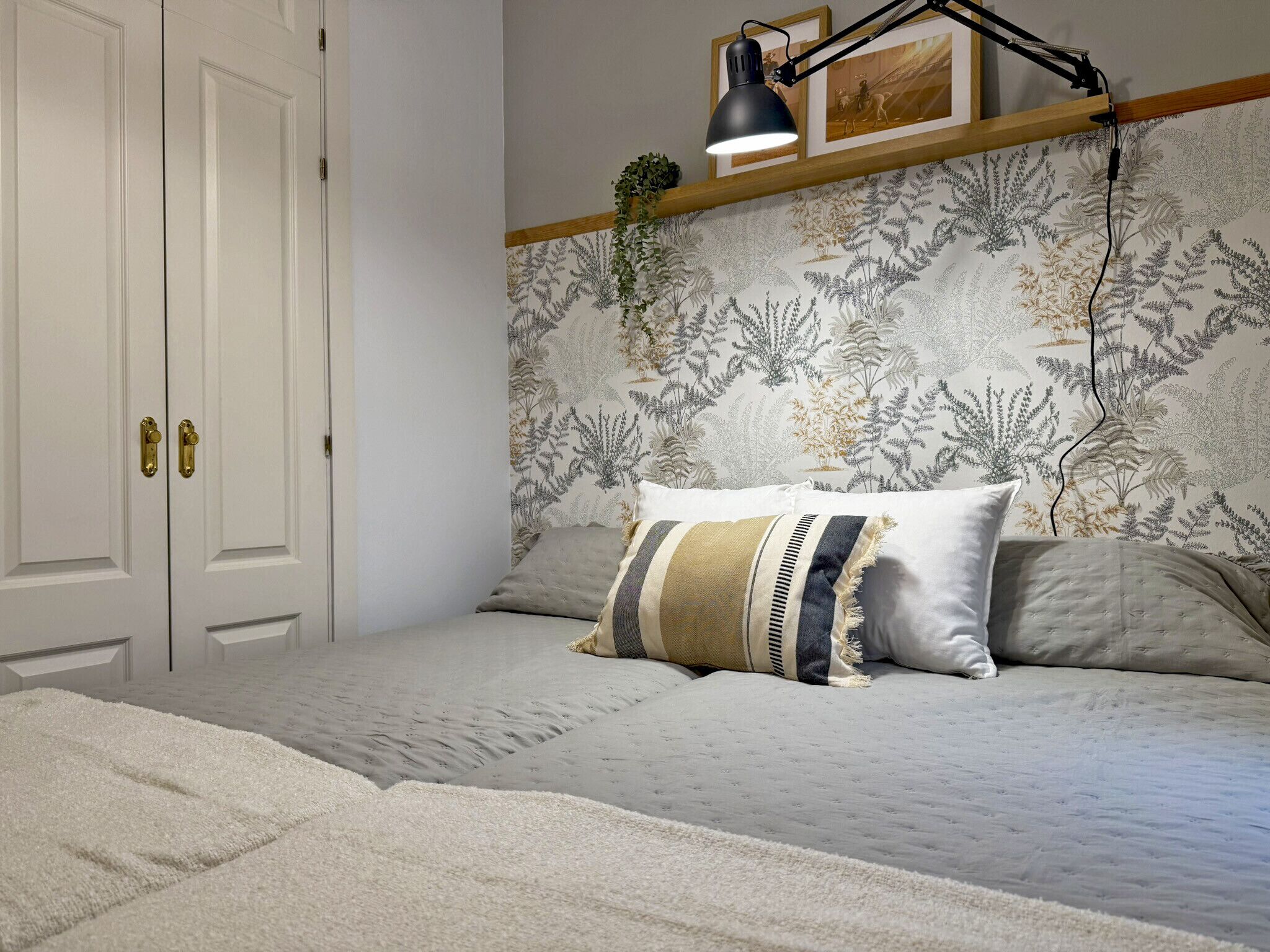 A bedroom with a bed, a nightstand, a desk lamp, a potted plant, and a door with a handle.