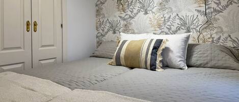 A bedroom with a bed, a nightstand, a desk lamp, a potted plant, and a door with a handle.
