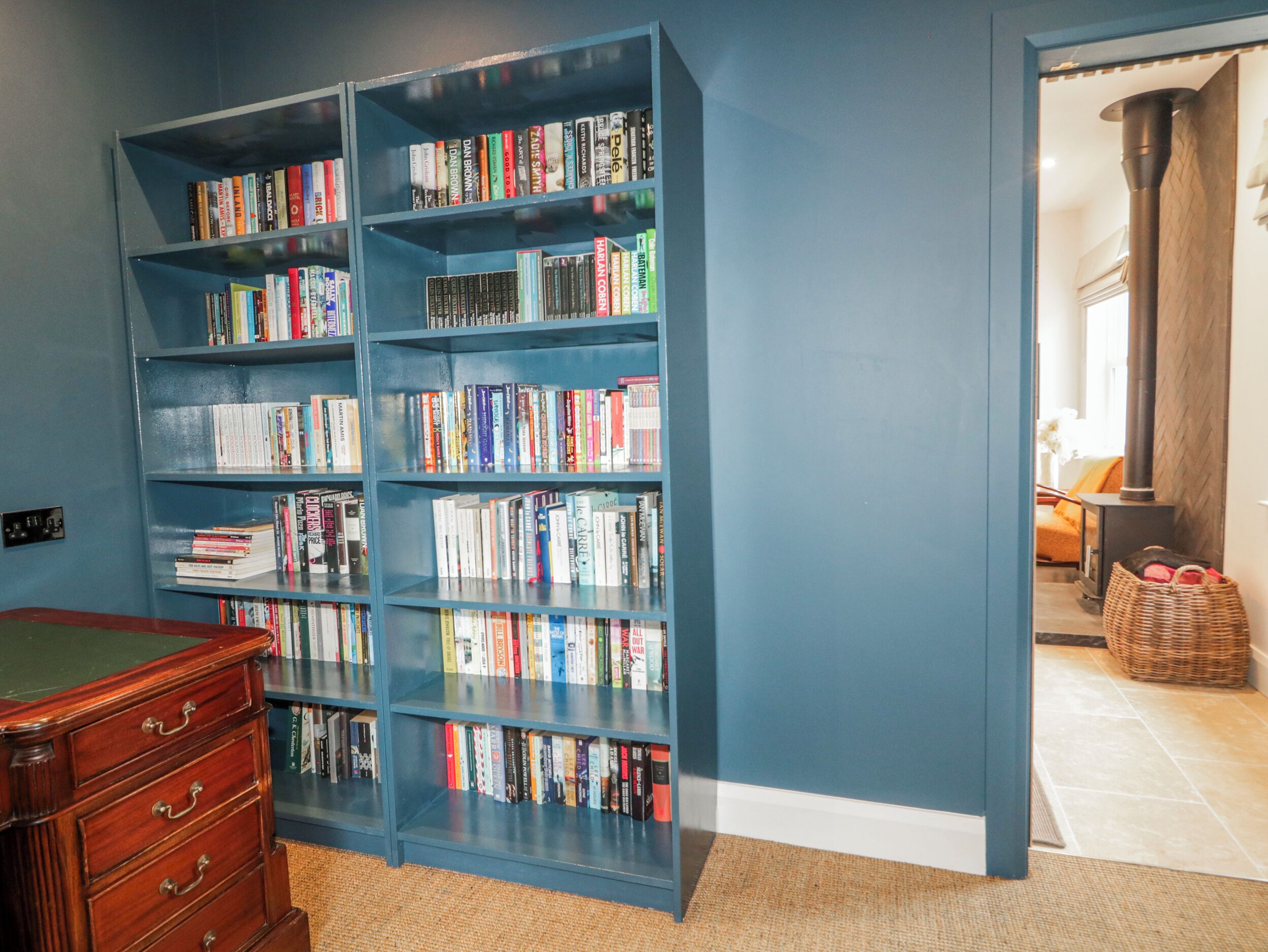 A room with a large blue bookshelf filled with books, a wooden dresser, and a wicker basket.