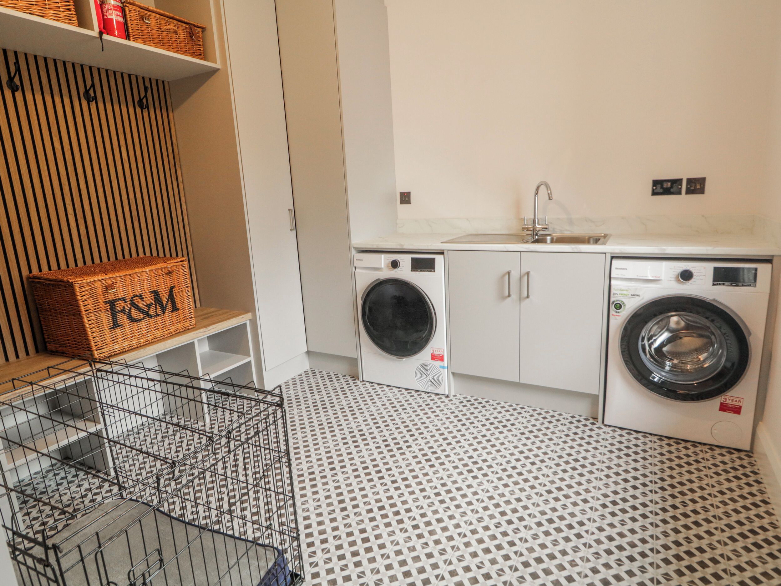 A laundry room with two washing machines, a sink, and storage shelves.