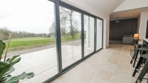 Interior moderno com grandes portas de correr de vidro, área de jantar com banquetas e vista para uma paisagem verde.