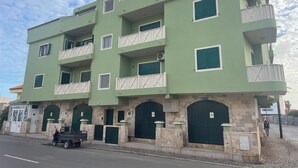 Ein mehrstöckiges Gebäude mit grüner Fassade, mehreren Balkonen und einem geschlossenem Eingangsbereich.