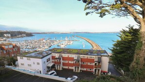 Un edificio costero con techo verde, junto a una marina con numerosos barcos.