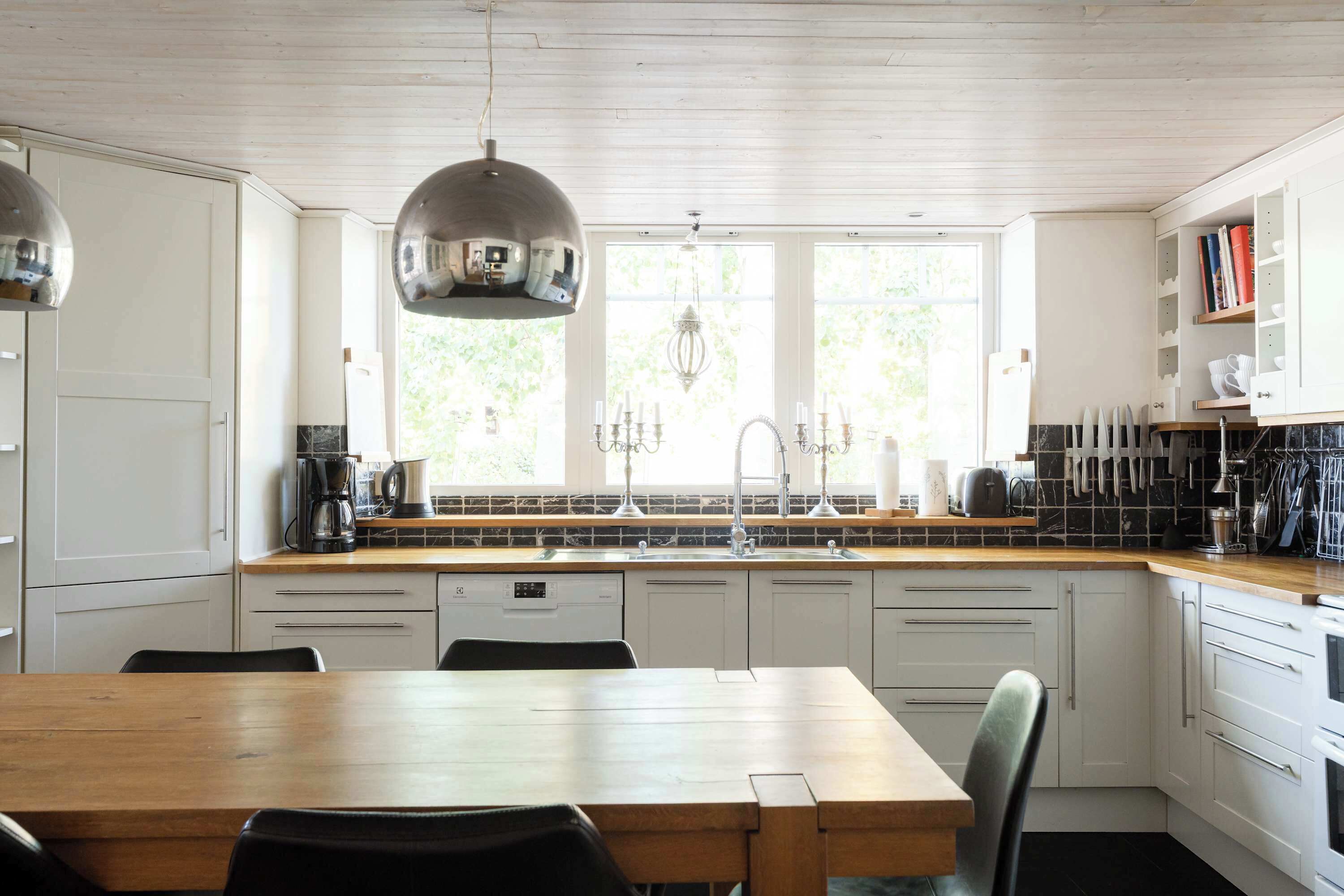 A modern kitchen with a wooden table, white cabinets, and a large window.