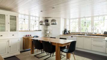 A modern kitchen with white cabinetry, a wooden dining table, black chairs, and a view of greenery outside.