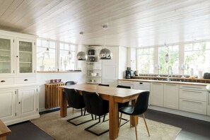 Een moderne keuken met witte kasten, een houten eettafel, zwarte stoelen en uitzicht op groen.