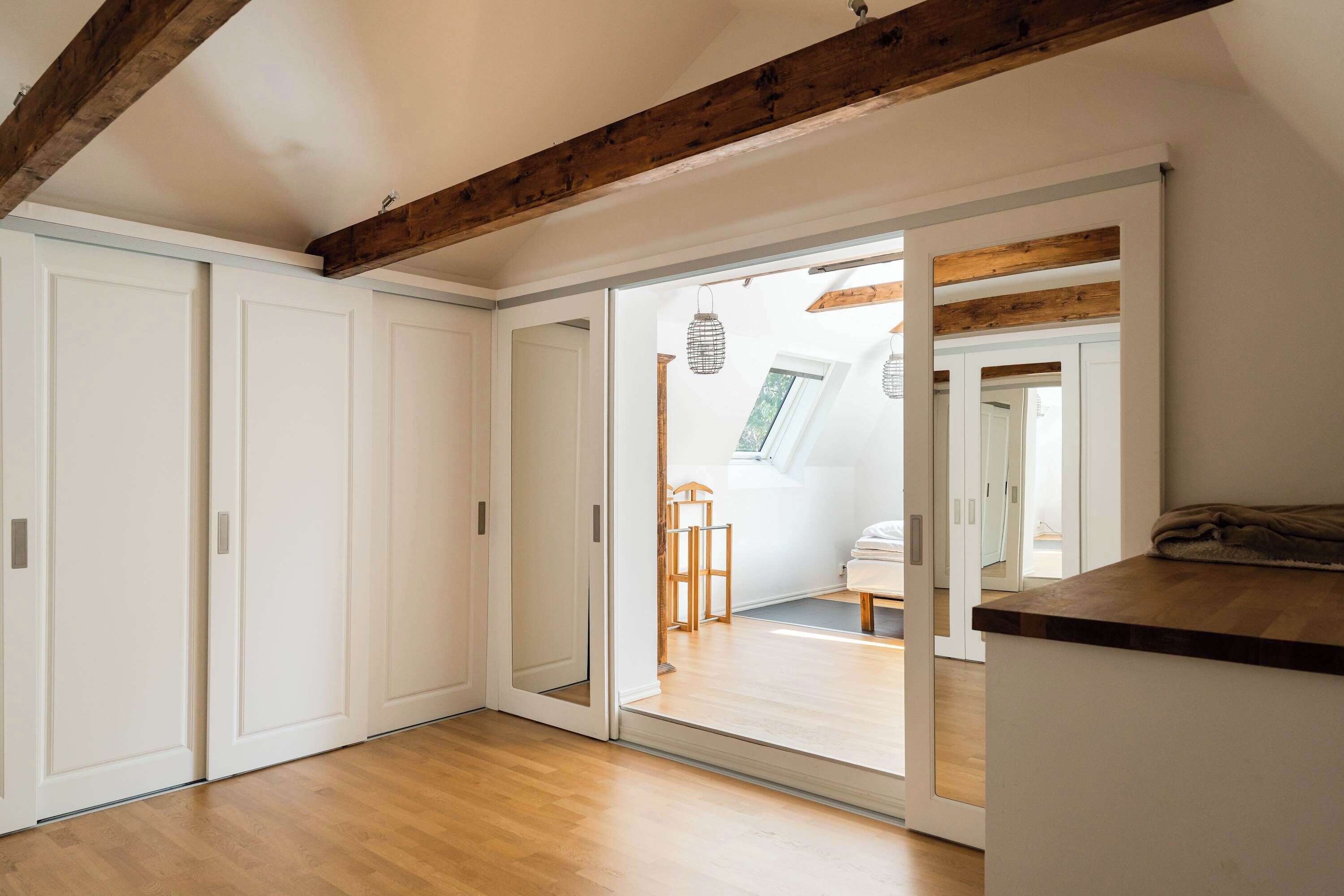 A room with a wooden floor, white walls, and a sliding door leading to another space.