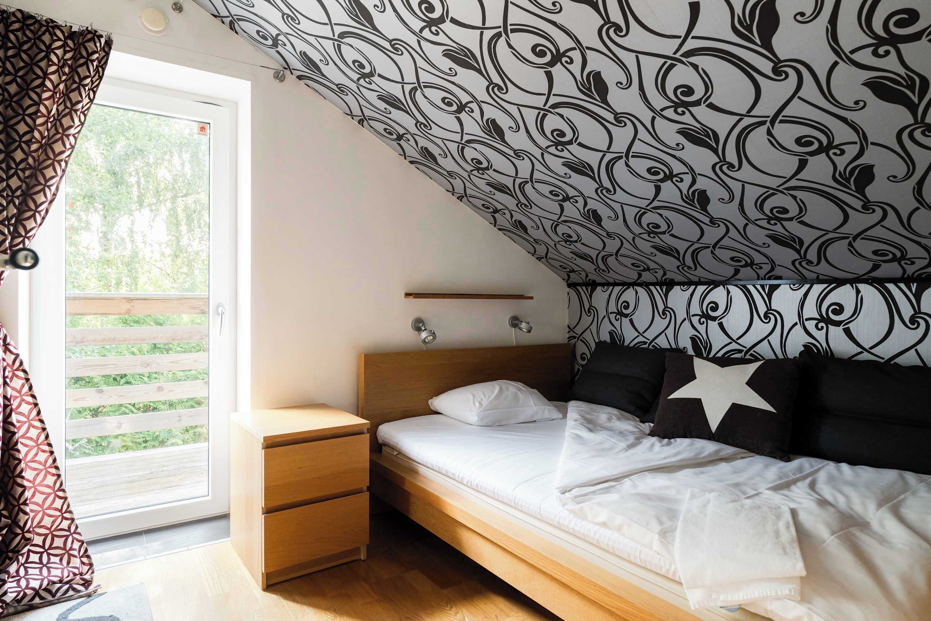 A bedroom with a sloped ceiling, a bed with white bedding, a nightstand, a drawer, and a wall-mounted lamp.