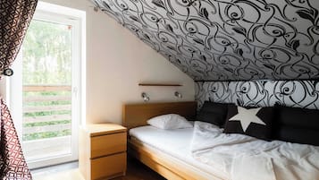 A bedroom with a sloped ceiling, a bed with white bedding, a nightstand, a drawer, and a wall-mounted lamp.