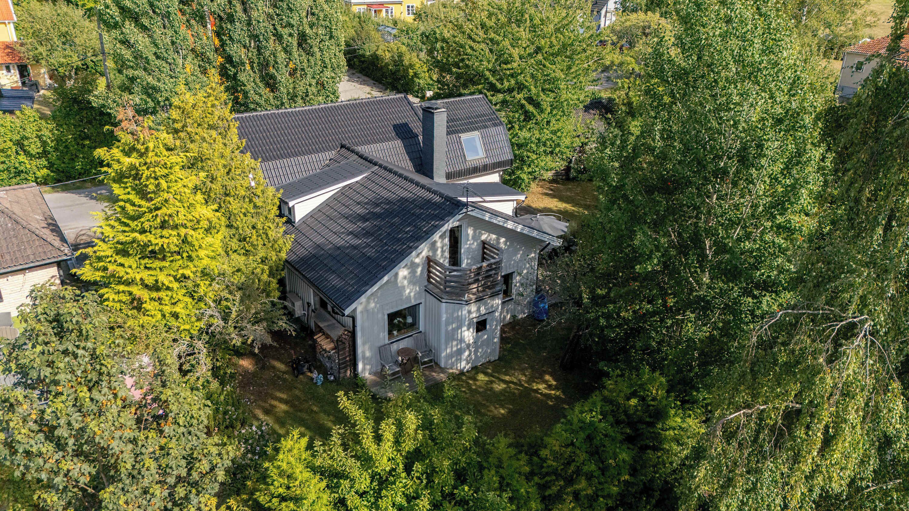 A two-story house with a dark roof, surrounded by dense greenery.