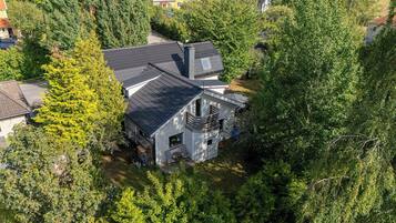 A two-story house with a dark roof, surrounded by dense greenery.