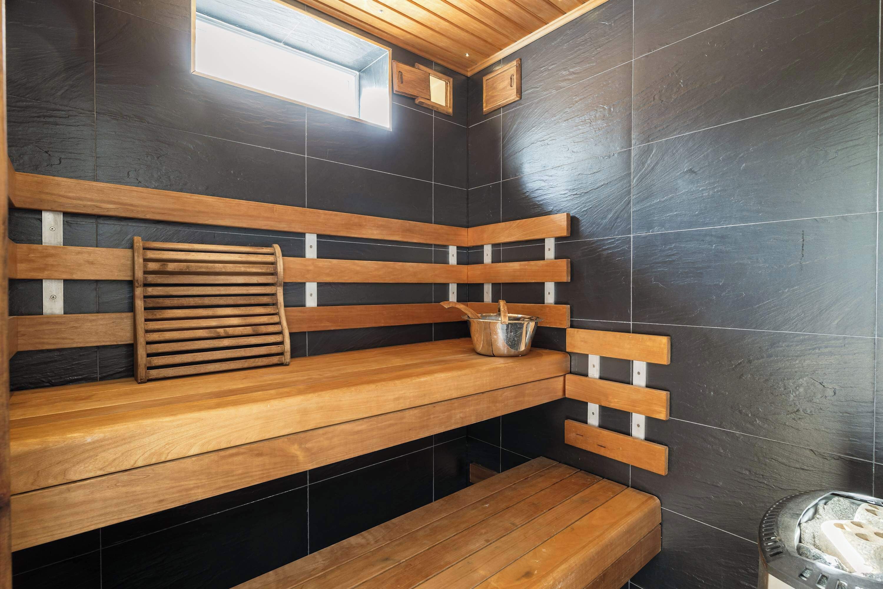 A sauna with wooden benches and a metal bucket.