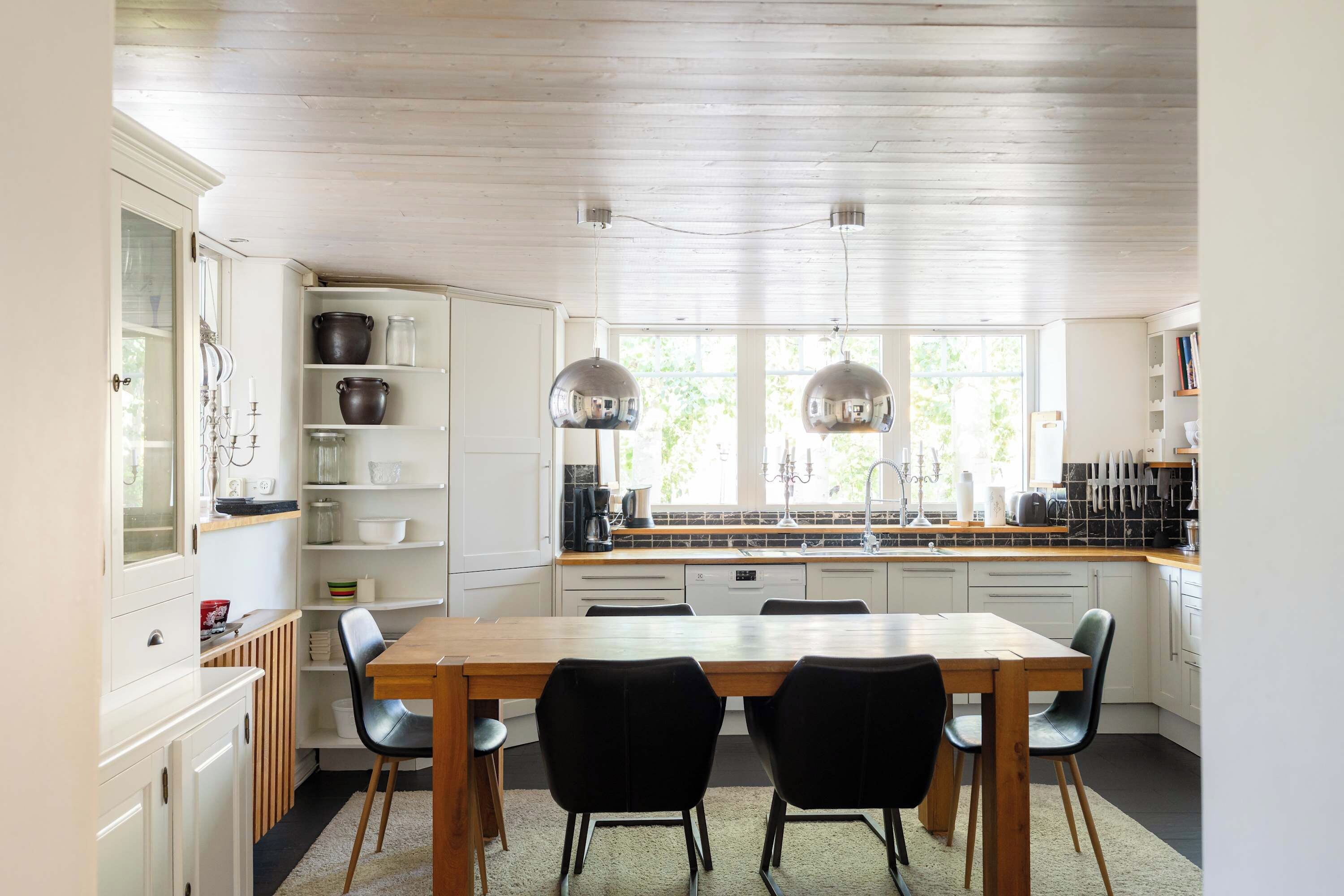 Een moderne keuken met witte kasten, een houten eettafel en zwarte stoelen.