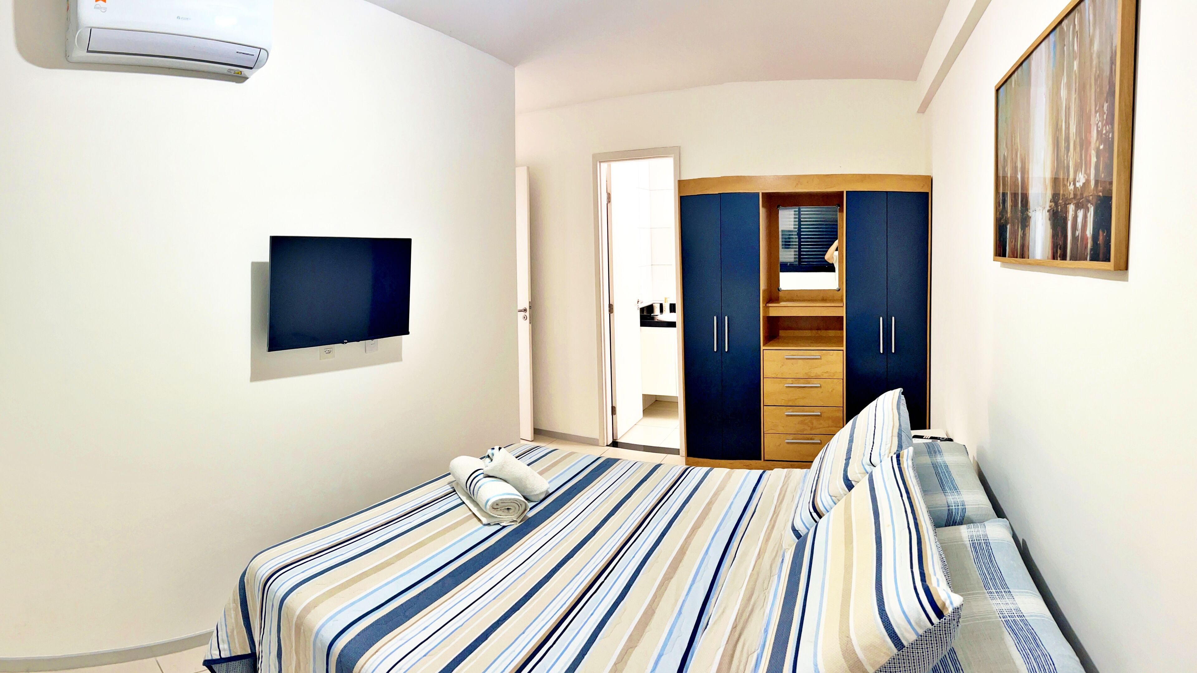 Un dormitorio con cama, televisión, armario y un cuadro.