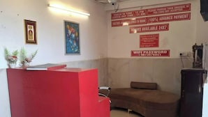 A reception area with a red desk, a couch, and a wall with informational signs including check-in/out times, advance payment, and WiFi password. - Hotel HR Residency (New Delhi)
