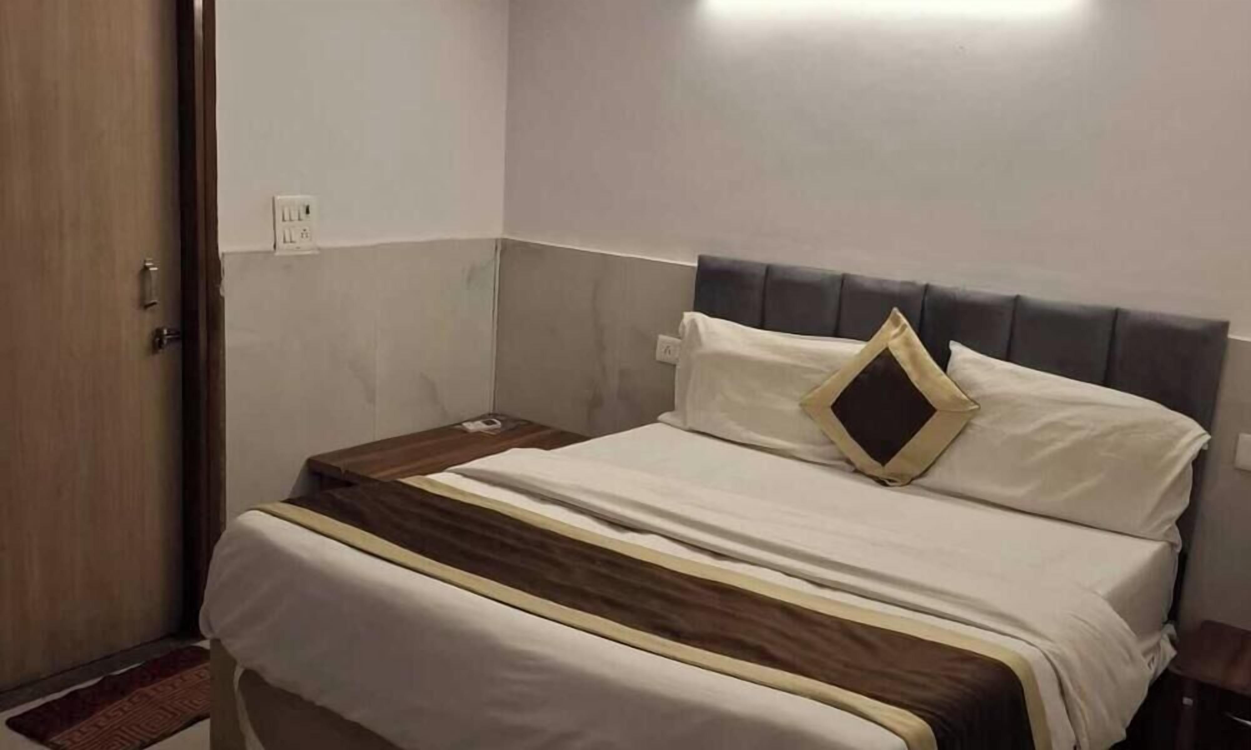 Una cama bien tendida con cabecera, una mesita de noche y un enchufe en la pared.