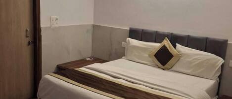Una cama bien tendida con cabecera, una mesita de noche y un enchufe en la pared.