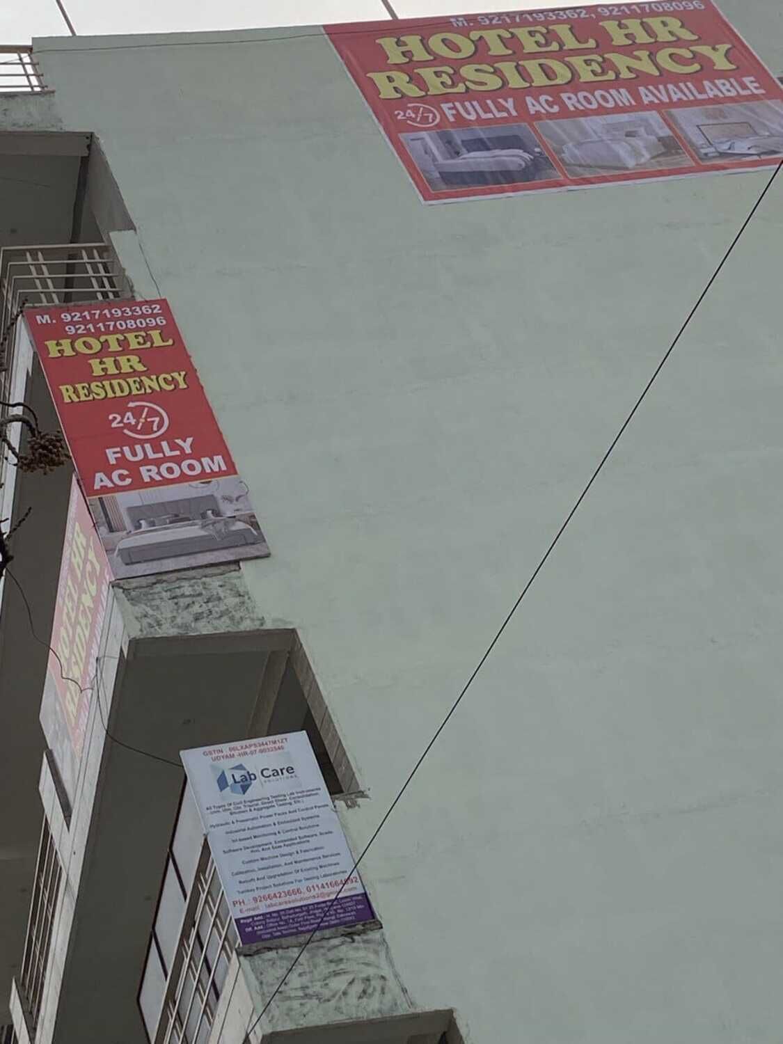 A building with multiple signs advertising a hotel HR residency with a 24/7 fully AC room available.