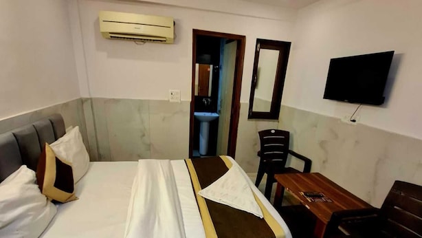 A hotel room with a bed, a desk, a chair, a television, and an air conditioning unit. - Hotel HR Residency (New Delhi)