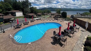Une piscine entourée de bâtiments, avec des chaises longues et des parasols, et offrant une vue sur un lac.