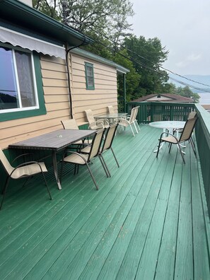 A covered outdoor deck with a table and chairs, a view of the water, and a small building with a green roof.
