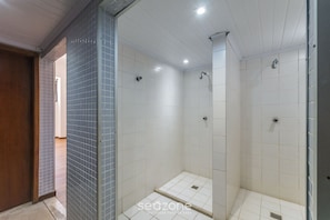 A bathroom with white tiled walls, a shower area, and a wooden door. - Apt With Balcony Steps From Barra Beach Tlr0113 (Salvador)