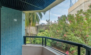 Un balcón con un muro de azulejos, barandilla de metal y vistas a vegetación y un edificio.