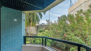 Un balcon doté d’un mur recouvert de carreaux, d’une rambarde en métal et offrant une vue sur la verdure et un bâtiment.