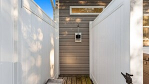 Un estrecho sendero de madera que lleva a una puerta con un buzón y un ventanal pequeño.