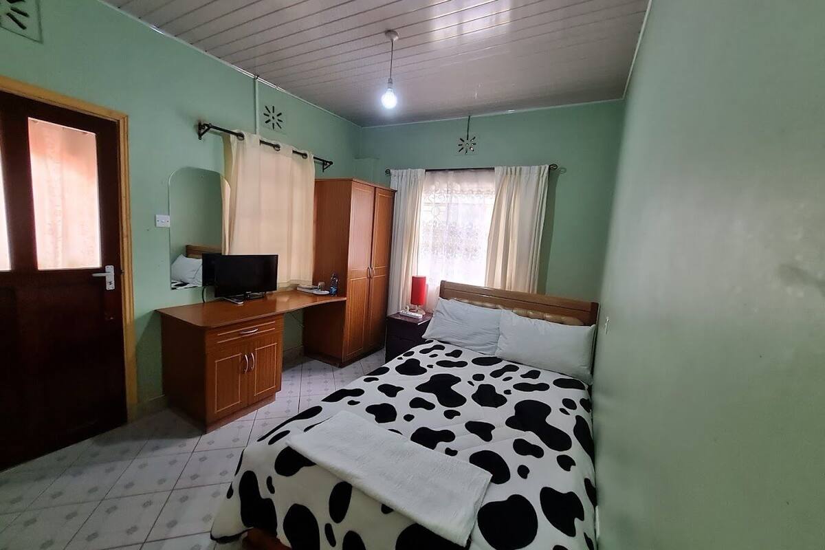 Un dormitorio con cama, escritorio, armario, televisor y ventana con cortinas.