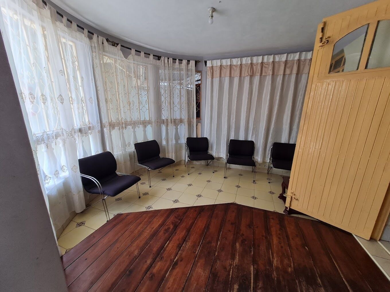A room with a curved wooden floor, four black chairs, and a wooden door with a window.