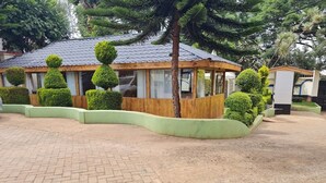 A building with a curved roof and a wooden facade, surrounded by neatly trimmed hedges and a paved walkway. - Queenspark Guest House (Nyeri)