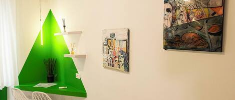 Una habitación con una pared verde decorativa, un escritorio con dos sillas blancas y dos obras de arte en la pared.