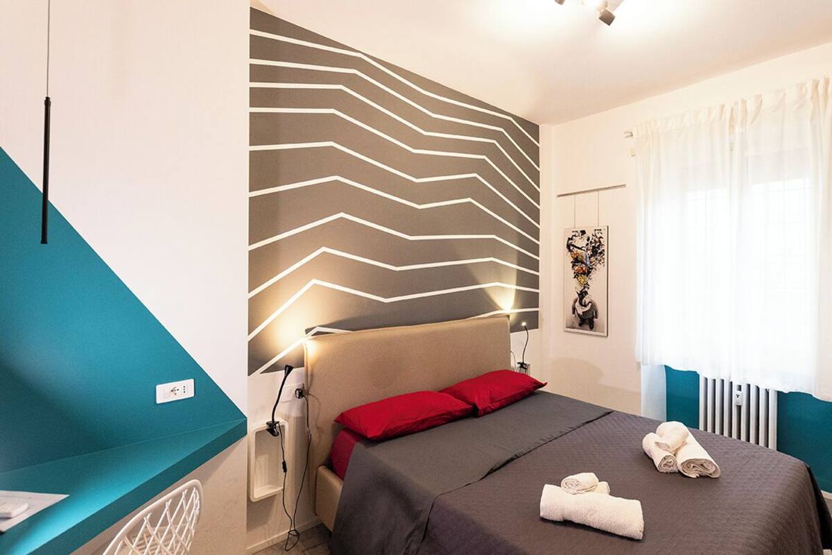 Une chambre d’hôtel moderne, équipée d’un lit, d’un bureau et d’un mur orné d’un motif en zigzag.